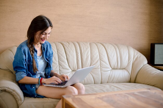 Senhora atraente usig laptop no sofá de couro