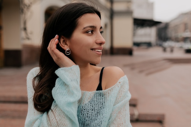 Senhora bonita encantadora com cabelo escuro e suéter menta posando sobre a cidade velha