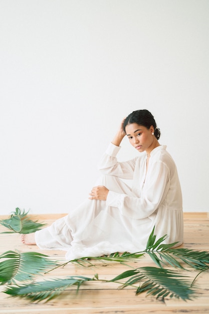 Senhora bonita no vestido longo branco sentado e olhando na sala vazia. espaço para texto