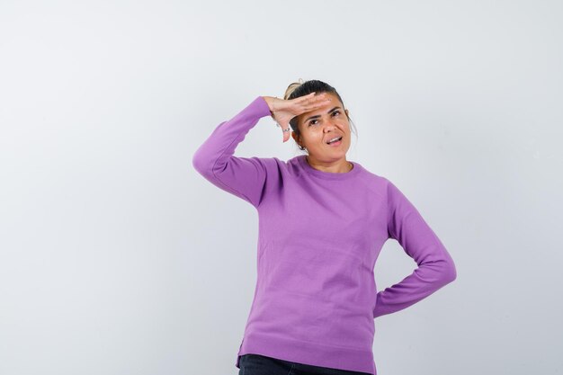 Senhora com blusa de lã olhando para longe com as mãos na cabeça e parecendo pensativa