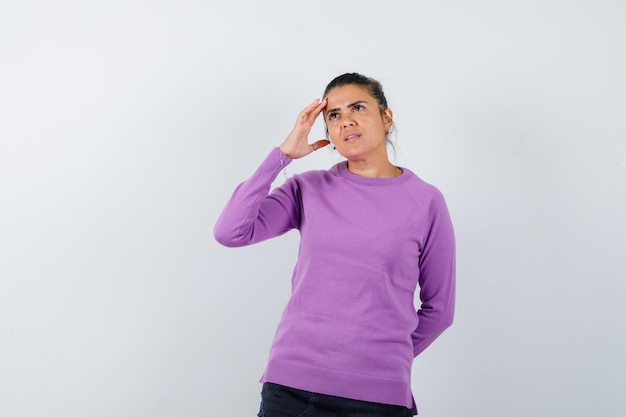 Senhora com blusa de lã segurando a mão na cabeça e parecendo sonhadora