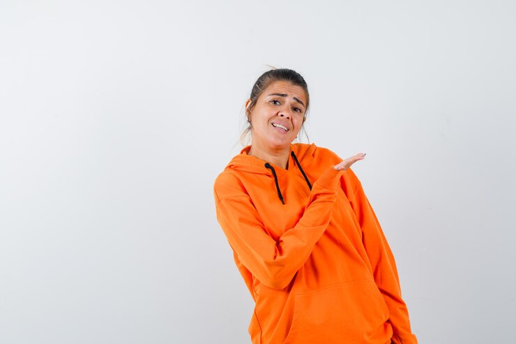 Foto grátis senhora com capuz laranja apontando para o lado e parecendo alegre