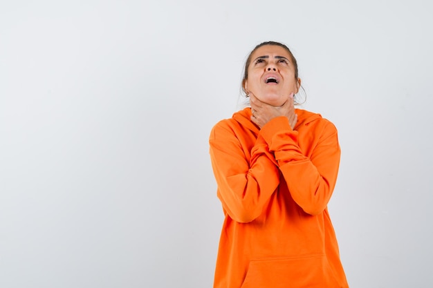 Senhora com dor de garganta usando um capuz laranja e parecendo doente