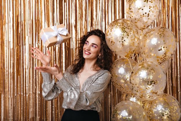 Foto grátis senhora de blusa prateada jogando uma caixa de presente sobre fundo dourado