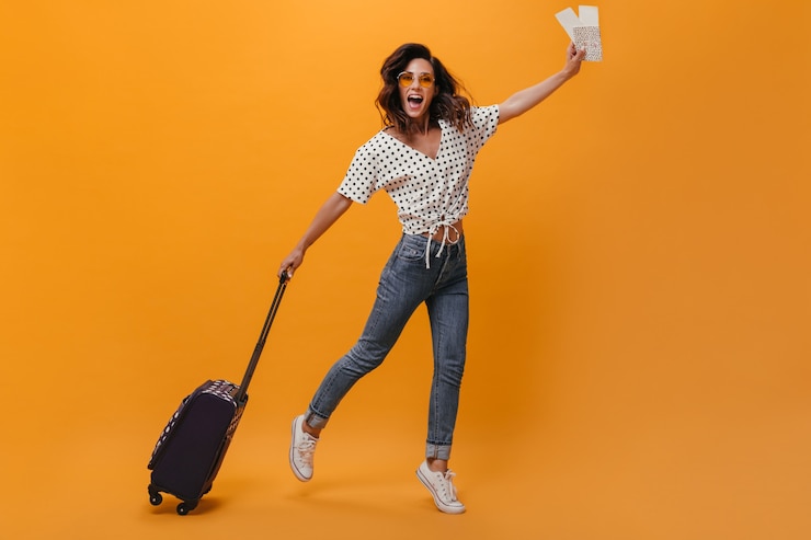 Foto grátis senhora de bom humor está pulando em um fundo laranja com ingressos e mala. divirta-se mulher feliz com cabelo curto ondulado em óculos de sol com tênis.