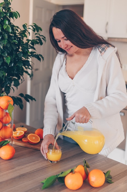 senhora de camisa branca e calça jeans derramando suco de laranja na cozinha