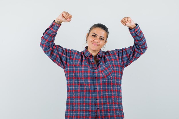 Senhora de camisa casual, mostrando o gesto do vencedor e olhando orgulhosa, vista frontal.