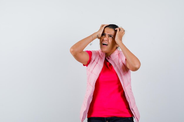 Senhora de camiseta, colete mantendo as mãos na cabeça e parecendo irritada