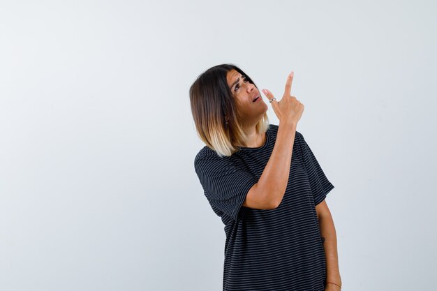 Foto grátis senhora de camiseta preta apontando para cima e parecendo esperançosa, vista frontal.