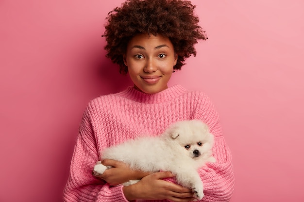 Foto grátis senhora de pele escura mantém os lábios arredondados, quer beijar bichinho adorável, brinca com cachorrinho