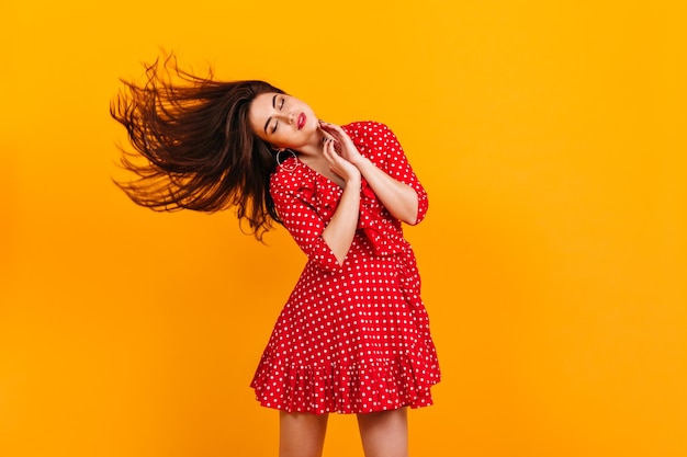 Foto grátis senhora de vestido polkadot está dançando em fundo amarelo retrato de modelo europeu tocando cabelo