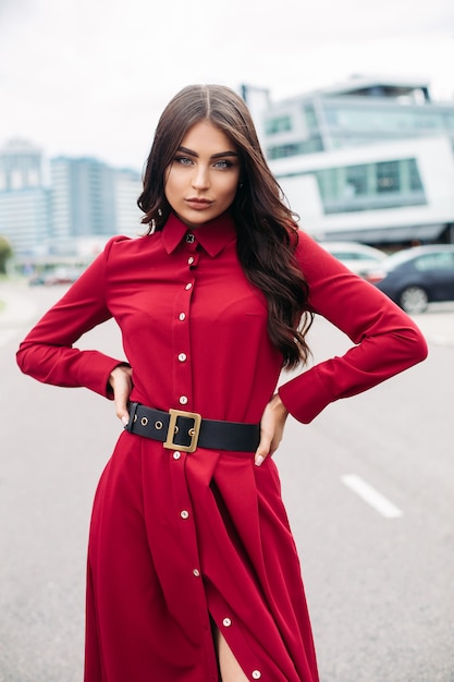 Senhora elegante confiante num vestido vermelho, posando para a câmera, segurando as mãos na cintura. moda feminina