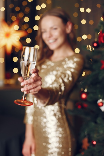 Senhora elegante perto da árvore de Natal. Mulher em casa com champanhe.