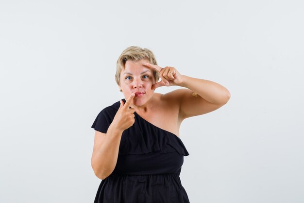 Senhora encantadora apontando para o lábio em blusa preta e parecendo concentrada