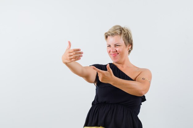 Senhora encantadora posando como se estivesse olhando a foto dela no telefone com uma blusa preta e parecendo satisfeita