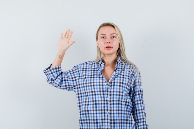 Senhora loira acenando com a mão para se despedir com uma camisa xadrez e parecendo confiante