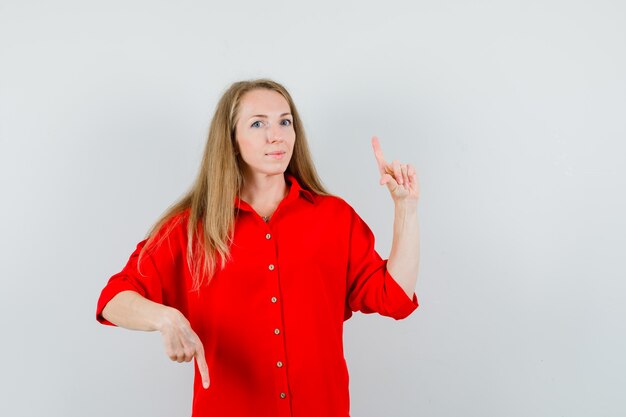 Senhora loira apontando os dedos para cima e para baixo na camisa vermelha e parecendo indecisa.