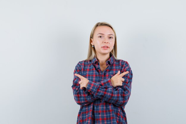 Senhora loira apontando para longe em uma camisa casual e olhando alegre, vista frontal.