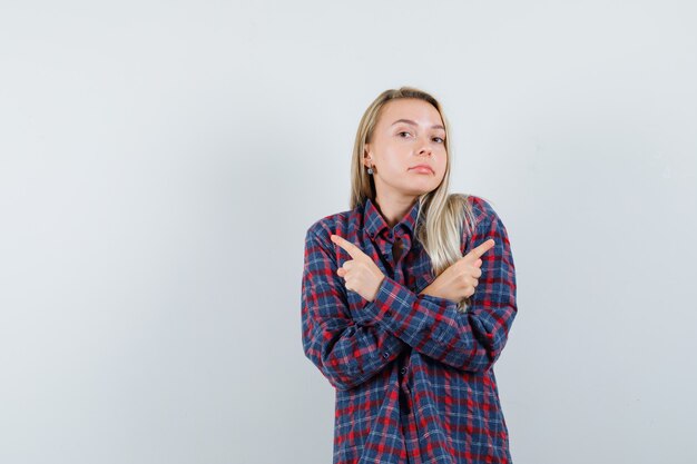 Senhora loira apontando para longe em uma camisa casual e parecendo confusa. vista frontal.