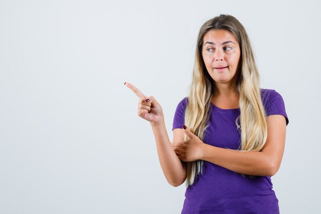 Senhora loira apontando para o canto superior esquerdo na vista frontal da camiseta violeta.