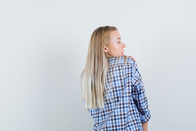 Foto grátis senhora loira com camisa casual, posando em pé e olhando atraente, vista traseira.