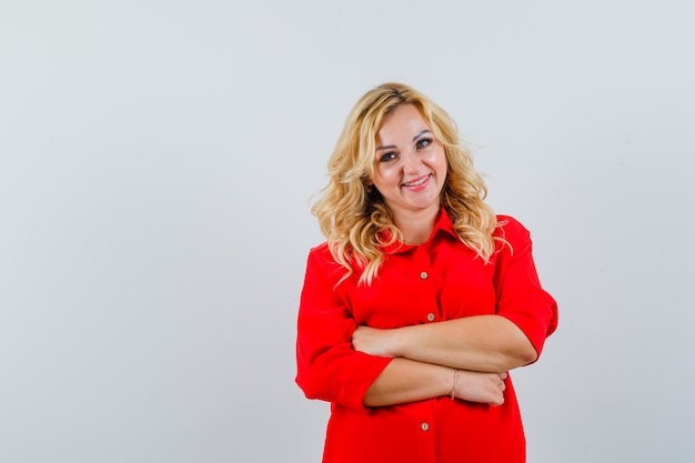 Senhora loira com os braços cruzados na camisa vermelha e parecendo otimista