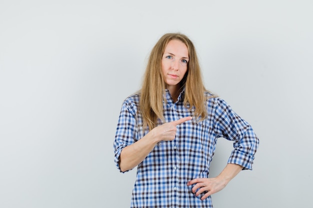 Senhora loira de camisa apontando para o canto superior direito e parecendo confiante,