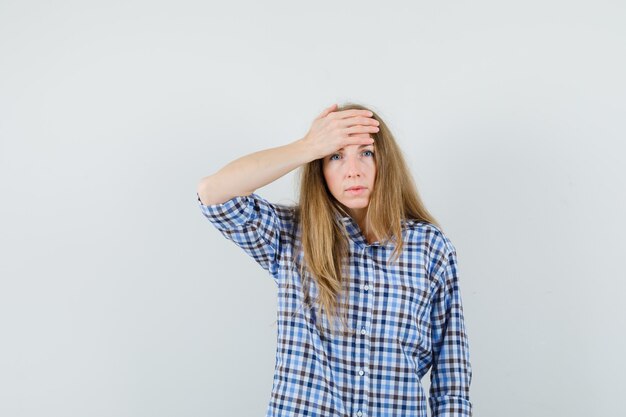 Senhora loira de camisa, segurando a mão na testa e parecendo triste,