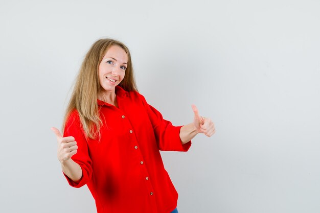 Senhora loira de camisa vermelha mostrando dois polegares para cima e parecendo alegre,