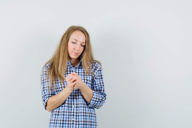 Senhora loira de mãos dadas na camisa e parecendo esperançosa,