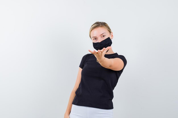 Senhora loira esticando a mão em direção à câmera em uma camiseta preta isolada