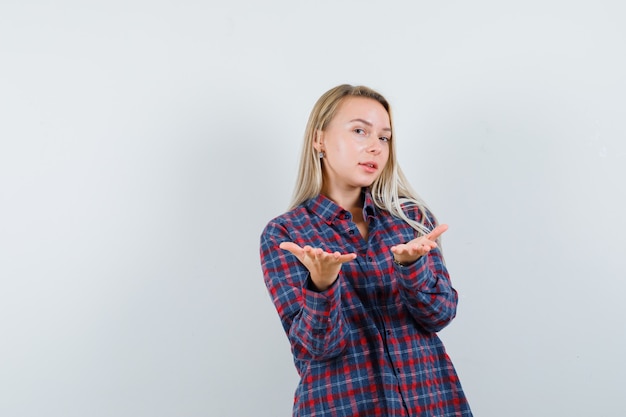 Senhora loira, esticando as mãos em uma camisa casual e olhando confiante, vista frontal.