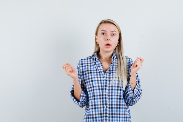 Senhora loira levantando as mãos em uma camisa xadrez e parecendo confusa