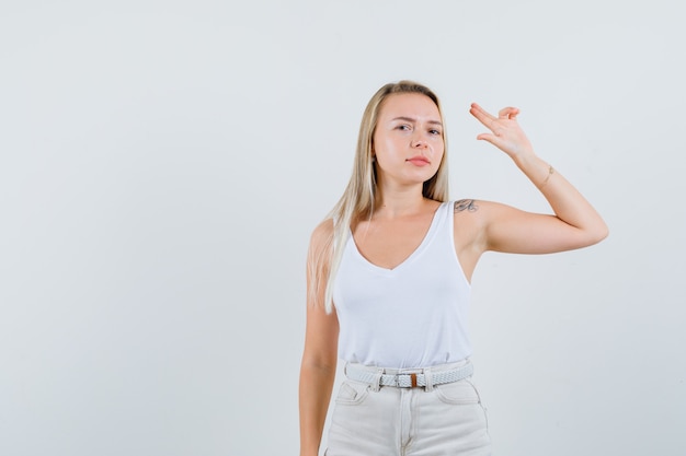 Senhora loira mostrando gesto de saudação em camiseta, calça e parecendo confiante