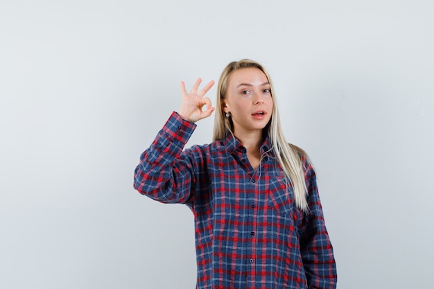 Senhora loira mostrando o gesto ok na camisa casual e olhando alegre. vista frontal.