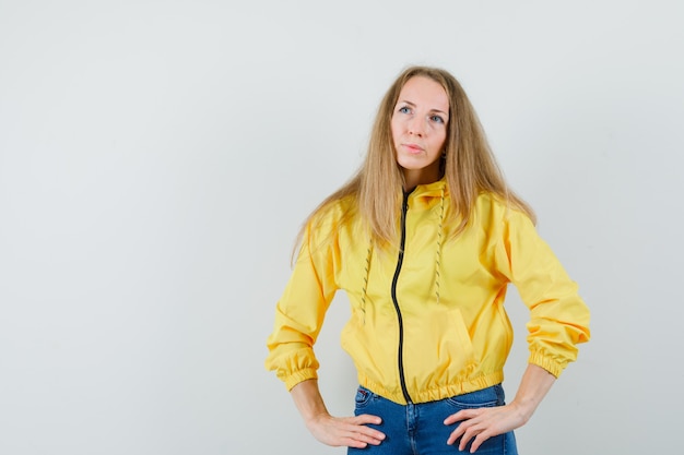 Senhora loira olhando para longe em jaqueta, jeans e parecendo pensativa,