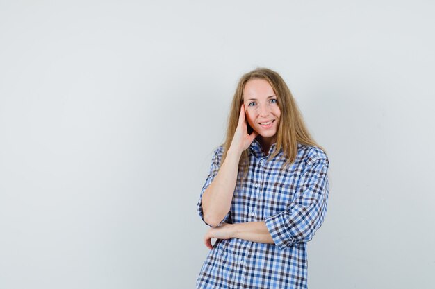 Senhora loira segurando a mão nas têmporas em uma camisa e parecendo alegre,