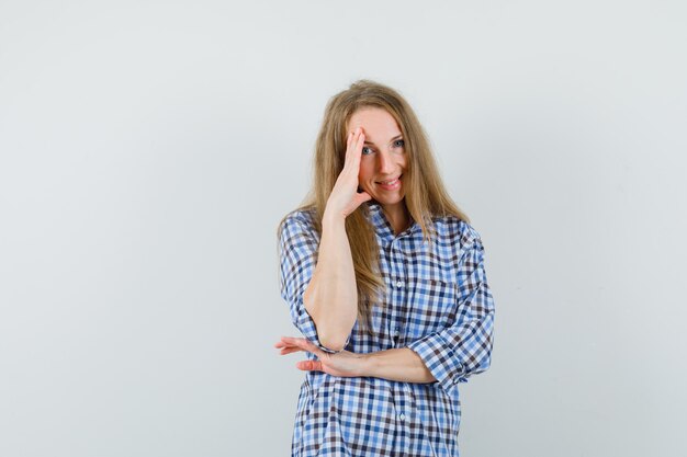 Senhora loira segurando a mão sobre o rosto em uma camisa e parecendo envergonhada,