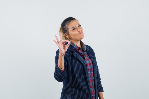 Senhora mostrando o gesto ok na camisa, jaqueta e olhando confiante, vista frontal.