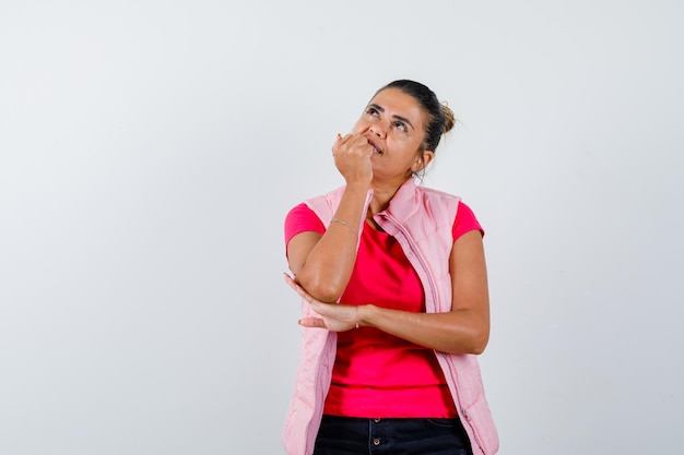 Senhora roendo as unhas em camiseta, colete e parecendo sonhadora