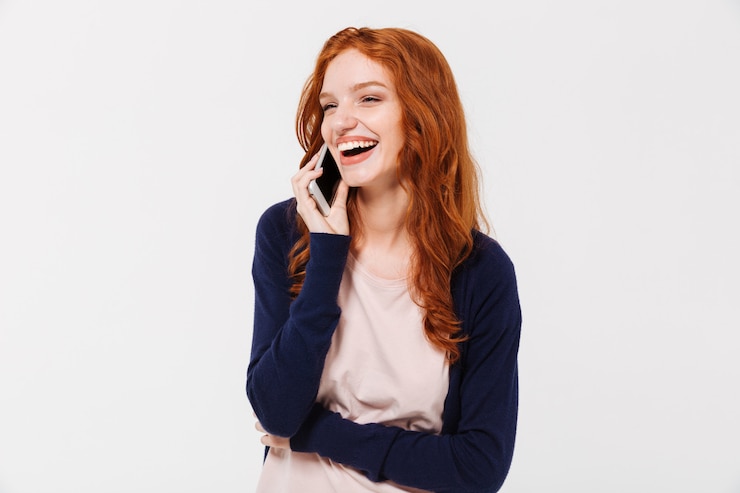 Foto grátis senhora ruiva jovem bonita alegre falando pelo telefone móvel.