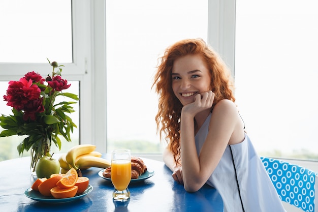 Senhora ruiva jovem muito alegre perto de flores e frutas