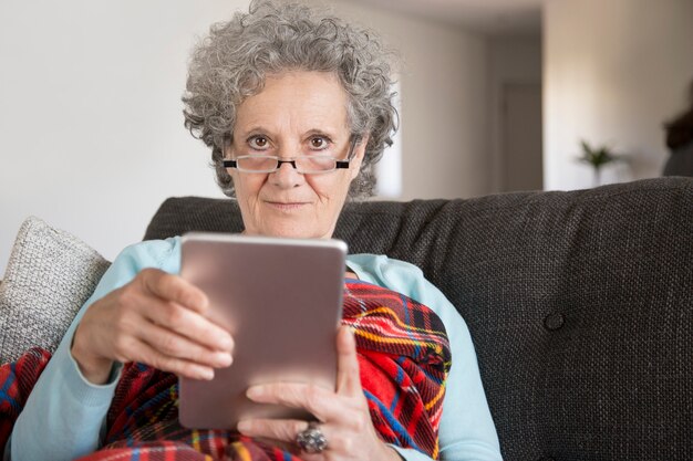 Senhora sênior de conteúdo com cabelo encaracolado, usando o dispositivo moderno em casa