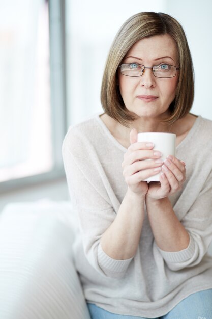 Senhora sentada no sofá com uma xícara de café