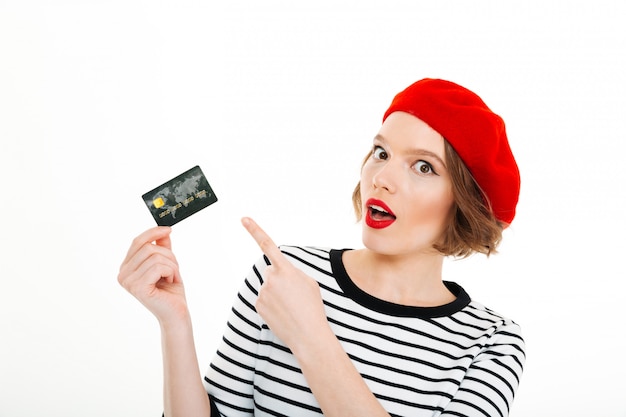 Senhora surpreendida séria que olha a câmera e apontando no cartão de crédito isolado