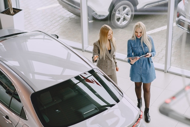 Senhoras em um salão de automóveis. Mulher comprando o carro. Mulher elegante com um vestido azul. O gerente ajuda o cliente.