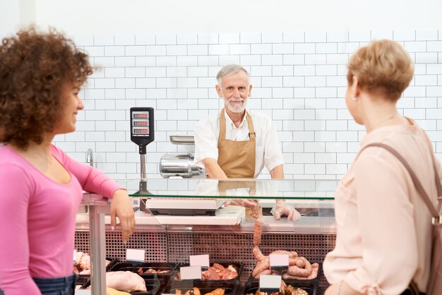 Senhoras, escolhendo produtos de carne crua atrás do balcão.