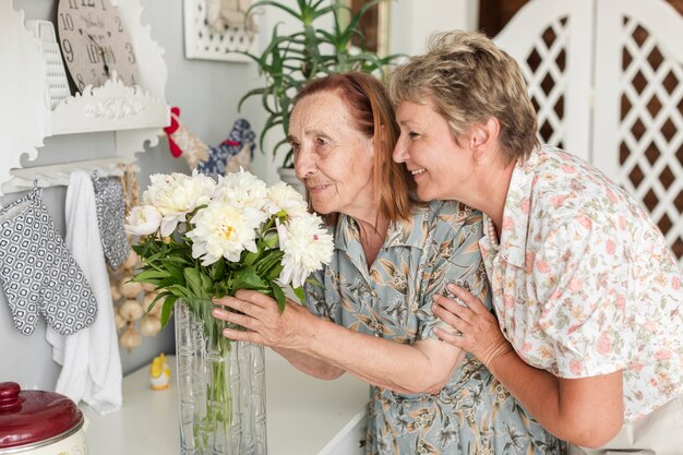 Sênior mãe e filha madura cheirando flores de vaso em casa