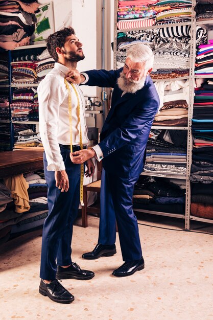 Senior masculino estilista tirar medidas de seu cliente na loja