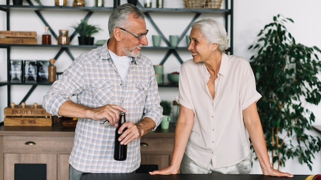 Foto grátis sênior mulher olhando marido abrindo a garrafa de cerveja na cozinha